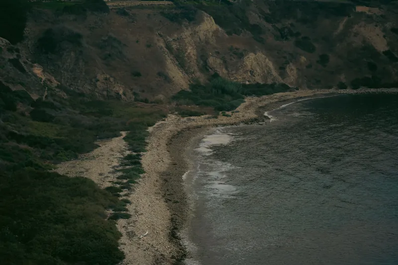 Serene coastal cliff with a pebble beach and calm waves in a natural setting.