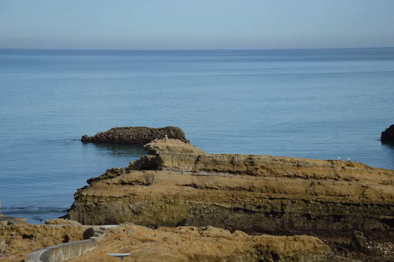 Peaceful coastal scene with eroded rock formations by the sea under a clear sky.