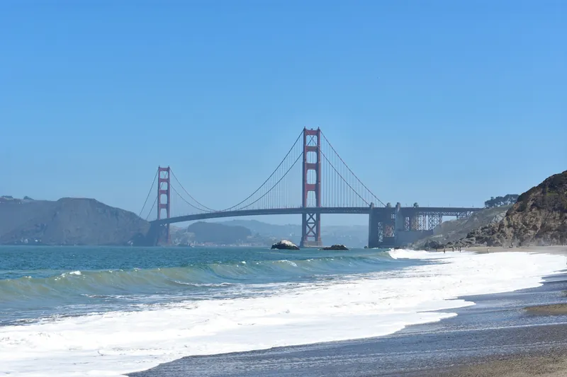 Scenic view of the Golden Gate Bridge with waves crashing on a sandy beach in San Francisco.