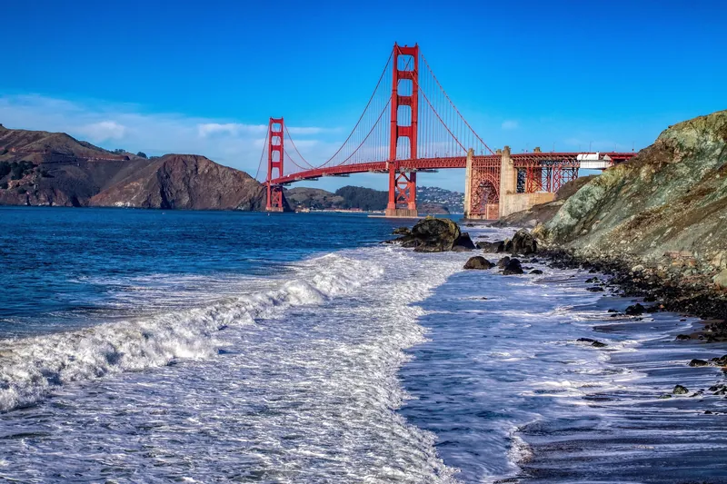Scenic view of the Golden Gate Bridge with crashing waves along the rocky San Francisco coastline.
