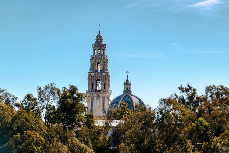 View of the California Tower at Balboa Park surrounded by trees under a clear blue sky.