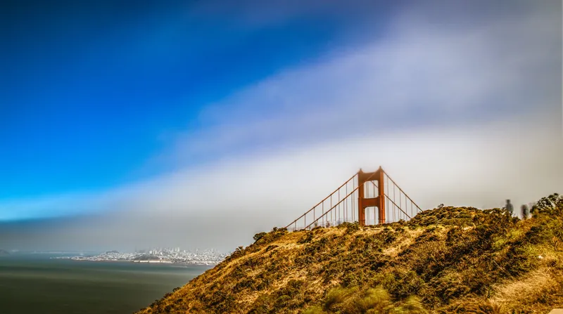 Iconic view of the Golden Gate Bridge framed by fog with San Francisco skyline in the background.