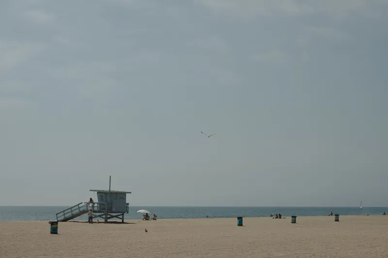 A peaceful beach scene featuring a lifeguard tower and scattered beachgoers under a clear sky.