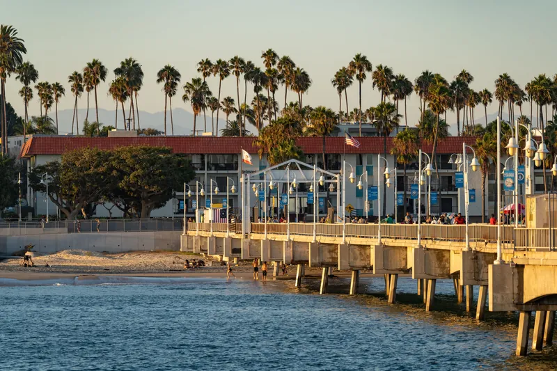 A serene view of Santa Monica Pier during sunset, featuring palm trees and beachgoers.