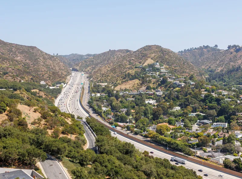 Aerial view of a busy Los Angeles freeway winding through picturesque hills and lush greenery.