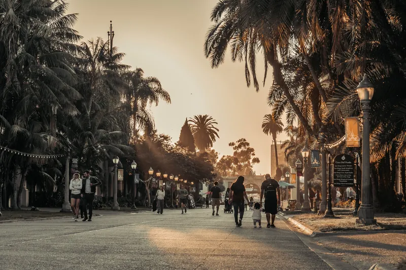 People walking under palm trees at sunset in San Diego's Balboa Park. Warm tones and relaxed atmosphere.