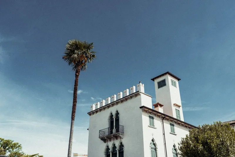 A picturesque villa beside a tall palm tree against a clear blue sky on a sunny day.
