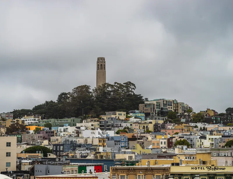 Panoramic view of San Francisco cityscape featuring the iconic Coit Tower under cloudy skies.