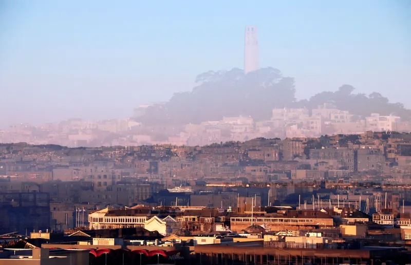 Stunning aerial view of San Francisco's iconic Coit Tower amidst a misty skyline at dawn.