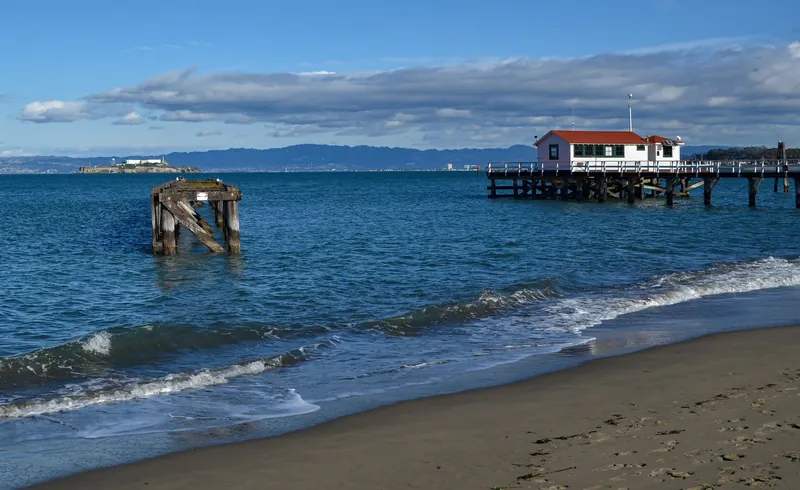 Serene shoreline view in San Francisco with Alcatraz Island, piers, and blue ocean under a cloudy sky.