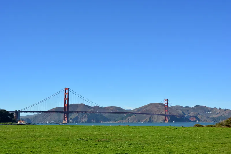 Golden Gate Bridge spanning San Francisco Bay on a clear day with grassy field in foreground.