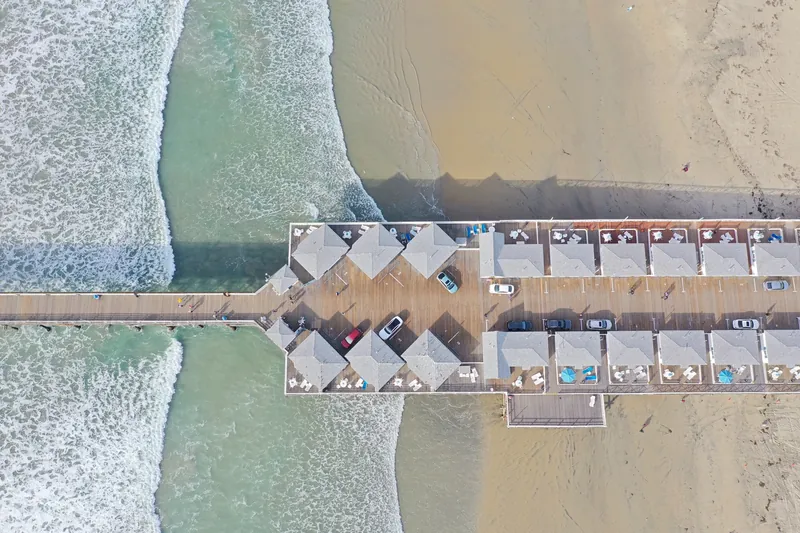Overhead view of a beach pier with cars, featuring waves and sandy shoreline in San Diego, CA.