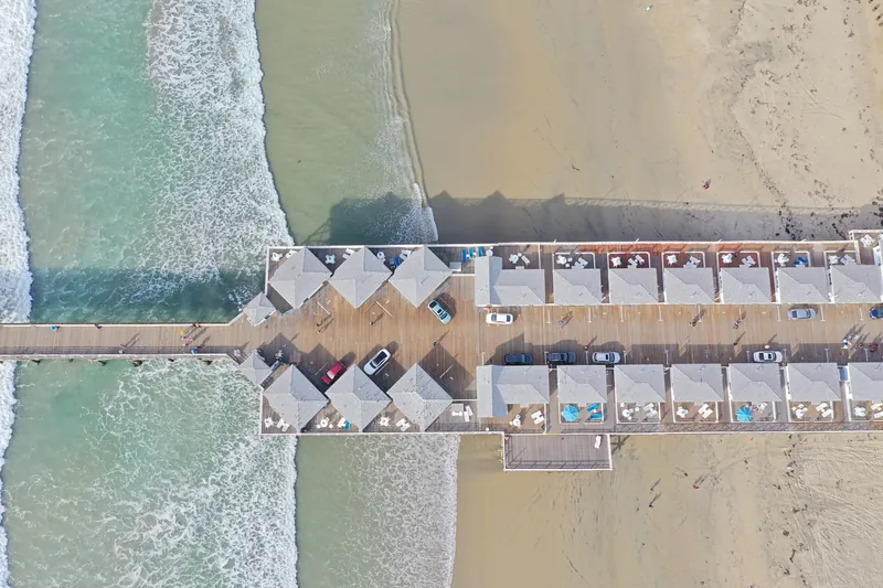 Stunning aerial photograph of a pier with cars and beach waves in San Diego, California.
