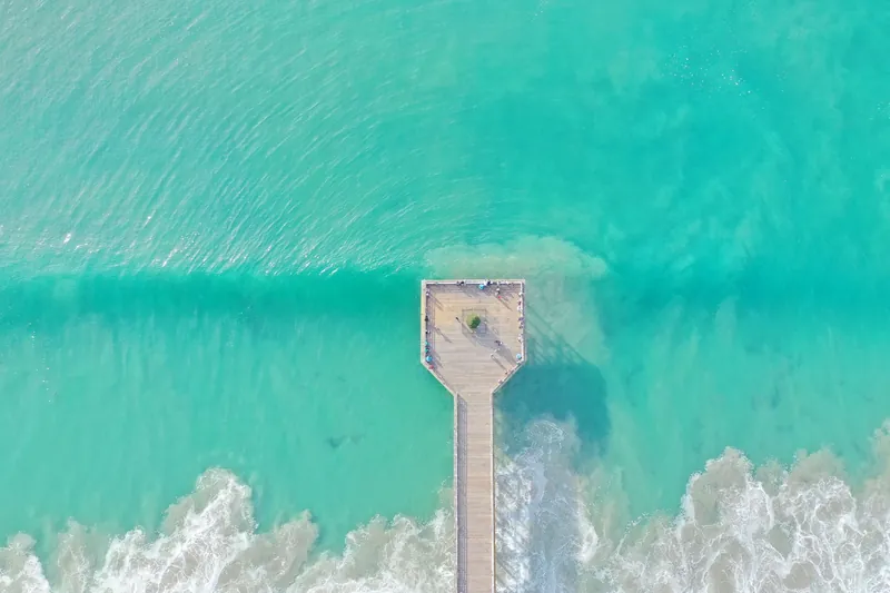 Drone shot of a pier extending into turquoise waters with gentle waves in San Diego, California.