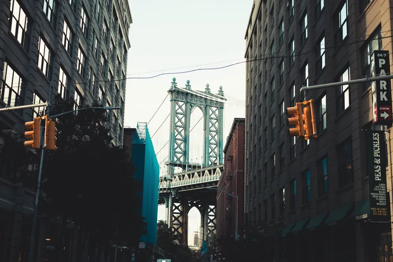 Scenic view of Manhattan Bridge framed by urban buildings in DUMBO, Brooklyn with traffic signals.