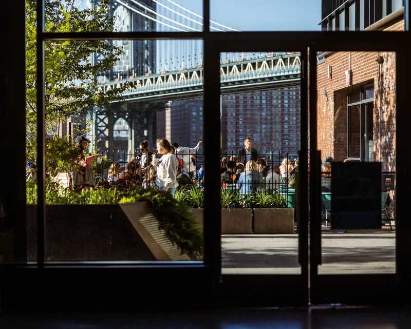 People gathering outdoors seen through a glass door with a bridge in the background.
