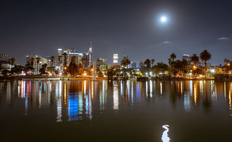 Stunning nighttime view of Los Angeles skyline with full moon reflecting on the waterfront.