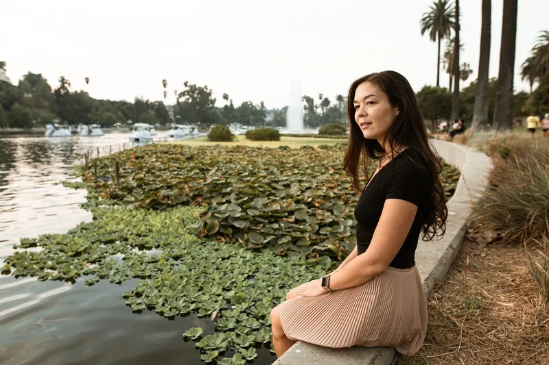 A woman sits by a serene lake filled with waterlilies, embodying tranquility.