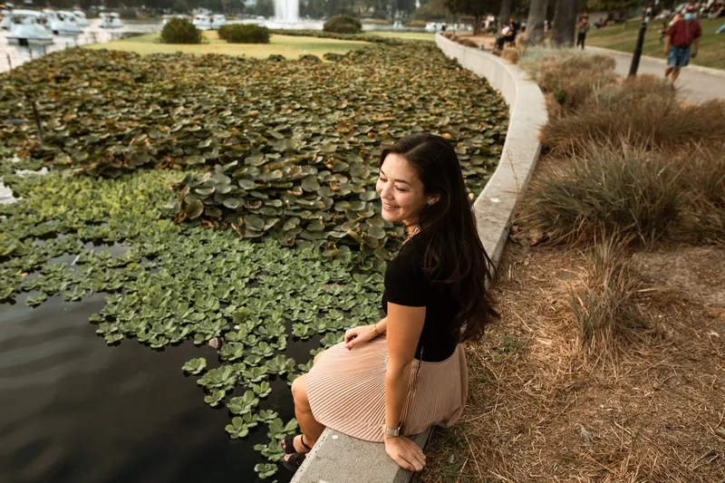 A calm woman sitting by a lake surrounded by greenery, embracing tranquility and self-care.