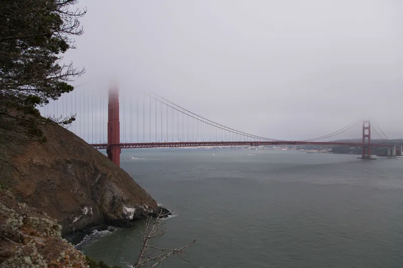 A foggy view of the Golden Gate Bridge with misty skies, seen from the San Francisco coastline.