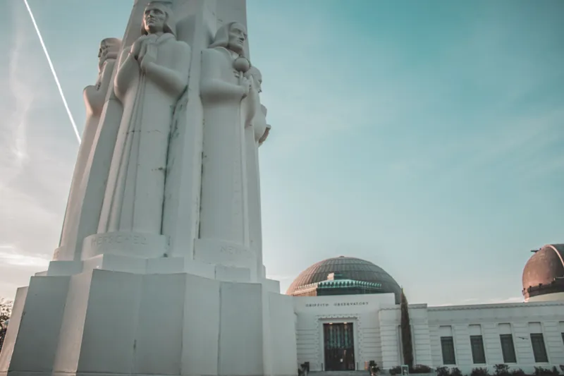 Low angle view of Griffith Observatory with Astronomers Monument, clear blue sky.