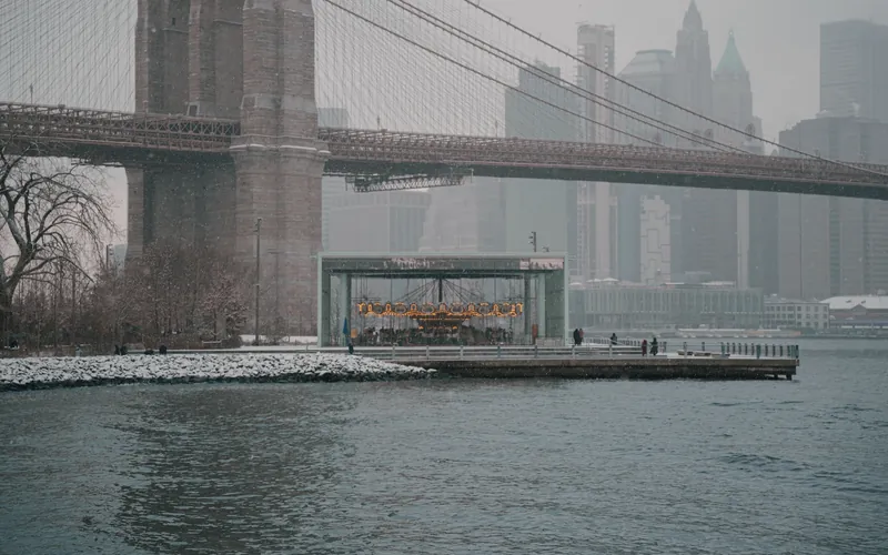 Snowy view of Brooklyn Bridge and Jane's Carousel in New York City during winter.