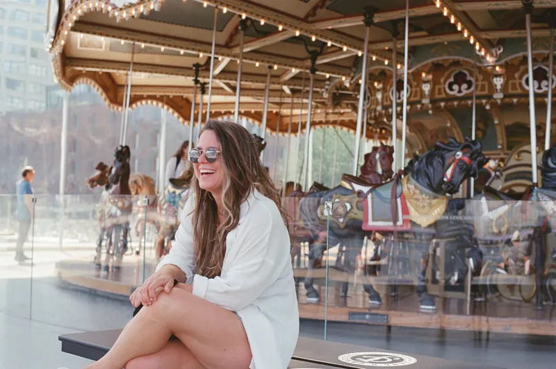 Caucasian woman laughing by a carousel in New York City during summer.