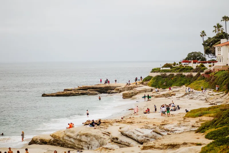 A vibrant and popular coastal scene on La Jolla beach with people enjoying the summer day.