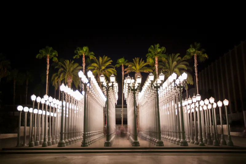 The Urban Light installation illuminating the night with palm trees in background.