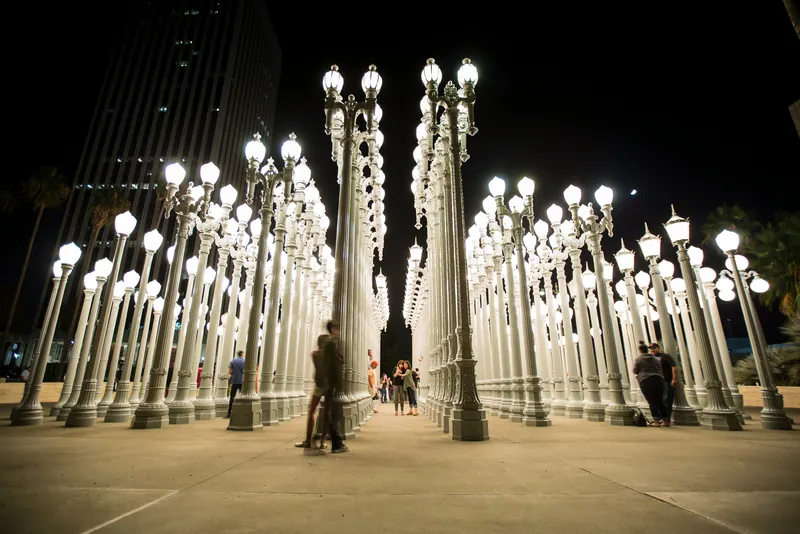 Nighttime view of the Urban Light installation at LACMA with visitors walking between the lit lampposts.