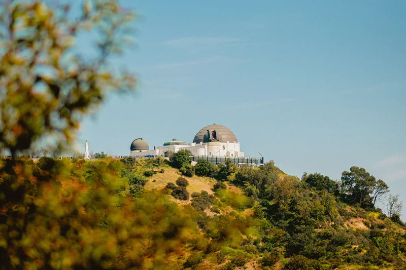 Scenic view of Griffith Observatory surrounded by lush greenery under a clear sky.