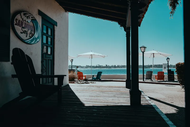 A serene beachfront view with shadows on a wooden deck and umbrellas by the water.