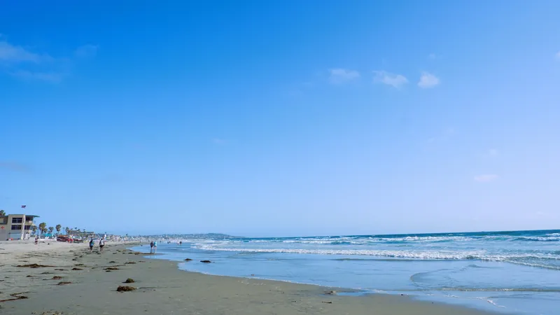 A peaceful view of a sandy beach in San Diego with blue skies and ocean waves.