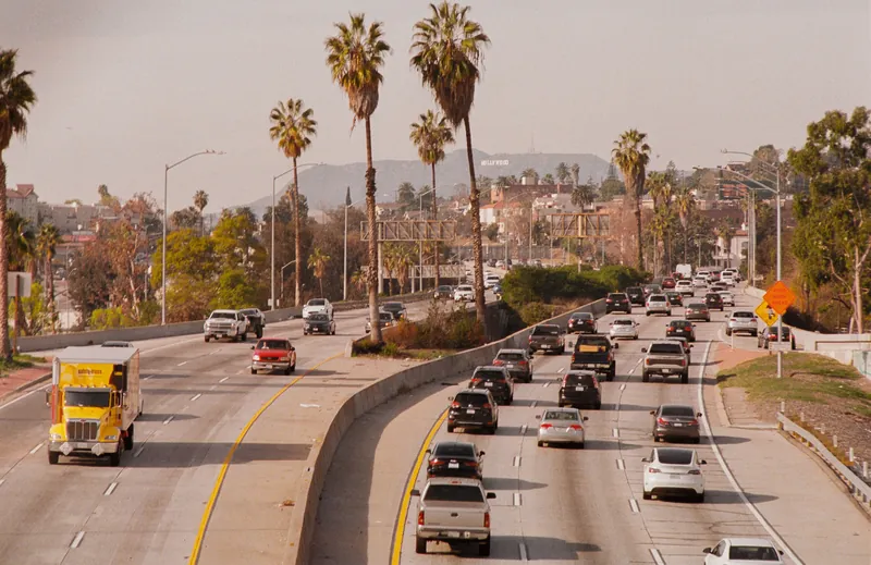 Busy highway traffic in Los Angeles with the iconic Hollywood sign visible in the background.