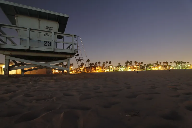 Lifeguard tower on a sandy beach at twilight, with city lights in the background.
