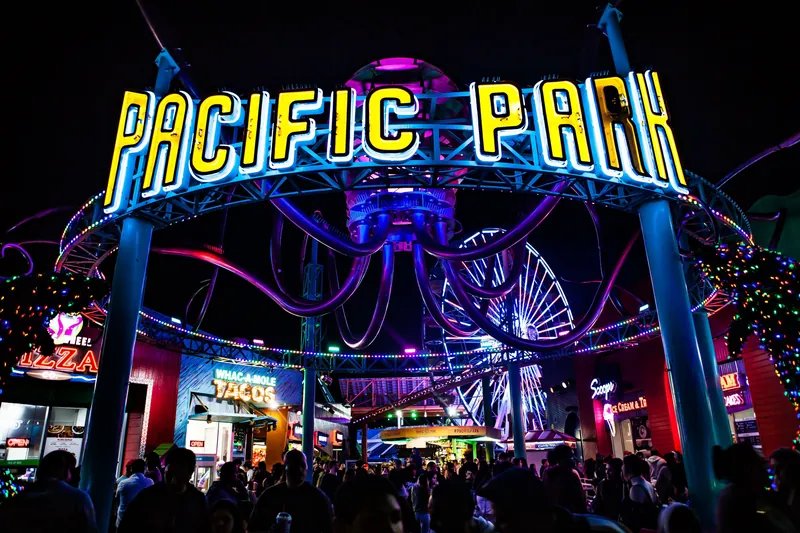 Colorful and lively night at Pacific Park with neon lights and a bustling crowd.