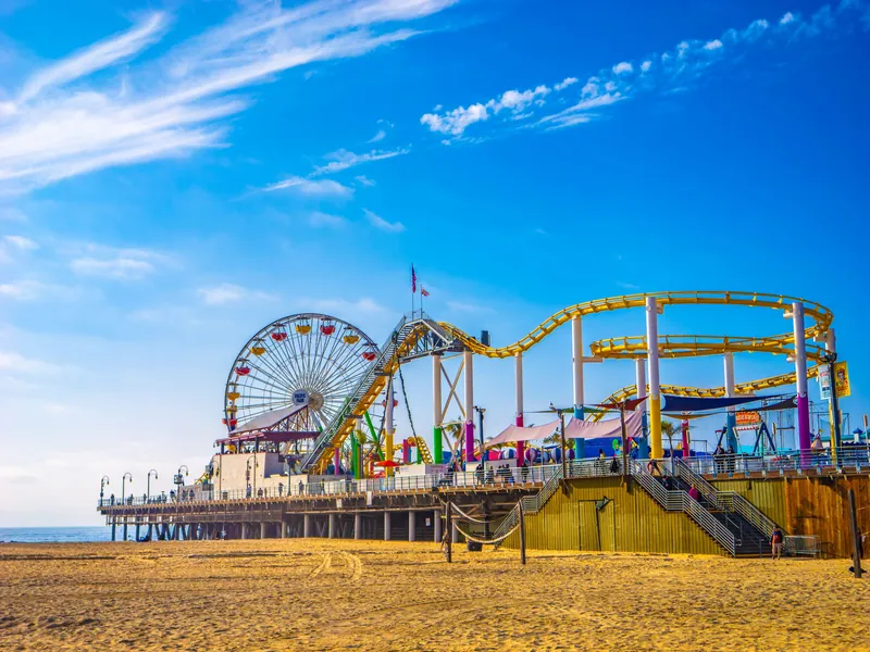 Colorful view of Santa Monica Pier with Ferris wheel and roller coaster under clear blue sky.