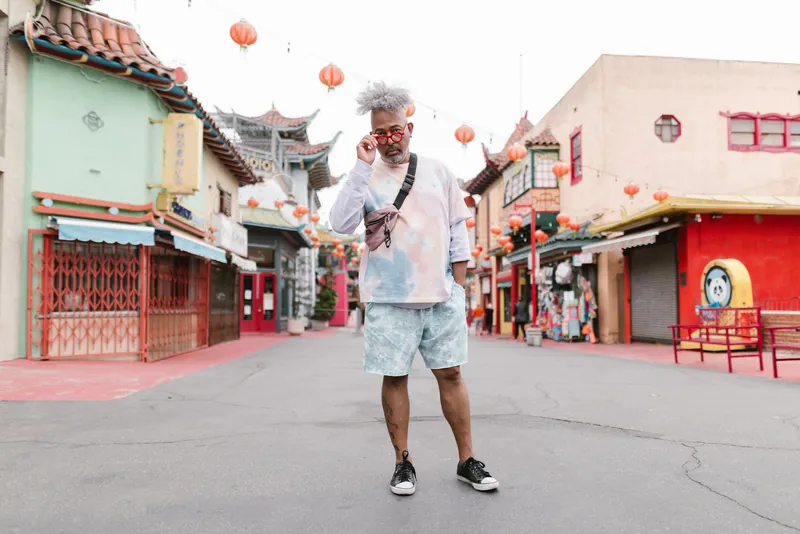 Fashionable man with afro hairstyle poses confidently in a colorful Chinatown setting, showcasing modern street style.
