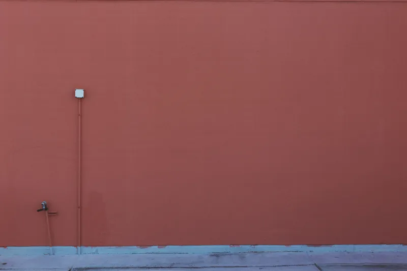 An orange-painted wall featuring a pipe and electrical outlet, perfect for minimalism themes.