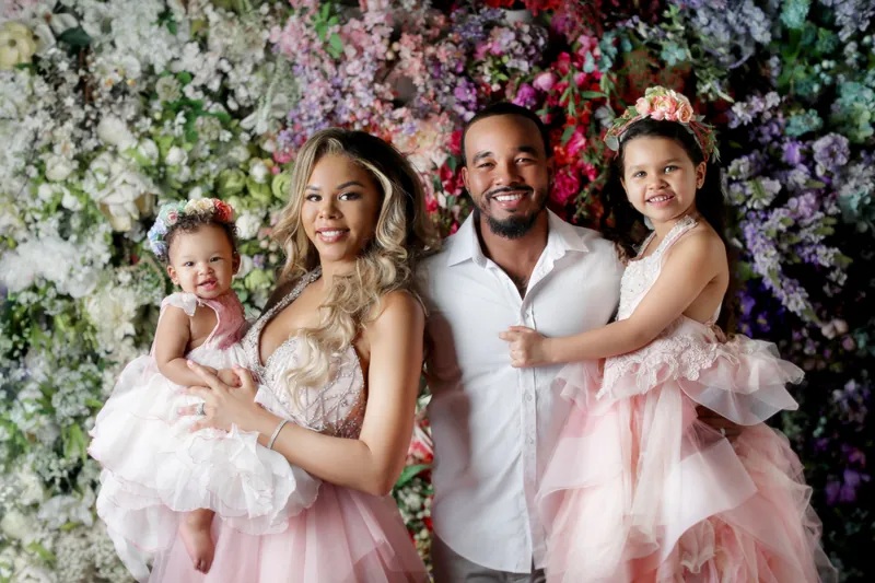 Charming family portrait with parents and children in pink attire against vibrant floral backdrop.