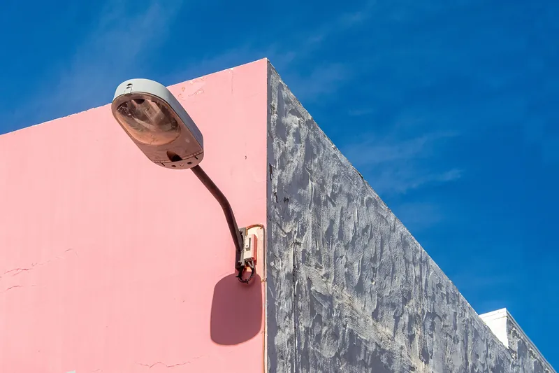 Street lamp on a colorful pink and gray building facade under clear blue sky.