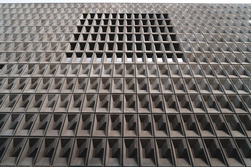 Concrete building facade with geometric patterns and recessed windows, showcasing modern architecture.