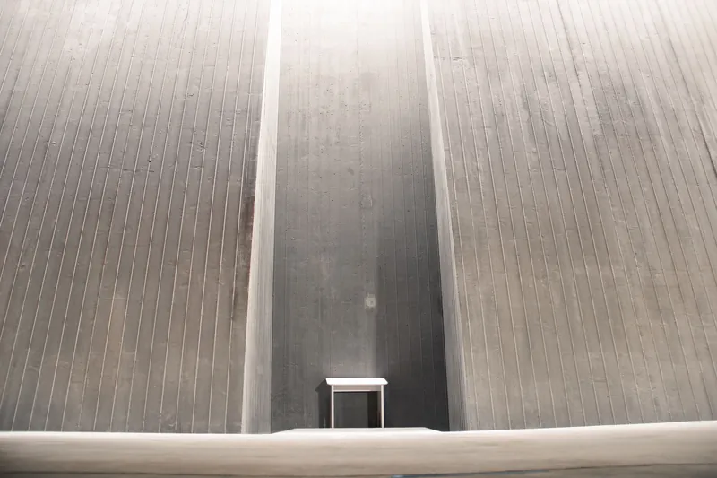 Minimalistic view of a solitary white table against textured gray concrete walls.