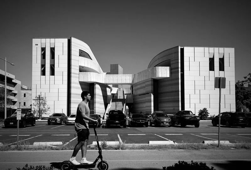 Black and white photo of modern architecture in San Diego with a man on a scooter in the foreground.