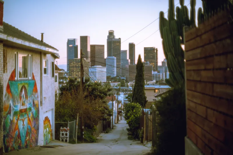Explore a colorful alley leading to Los Angeles skyscrapers at dusk, showcasing urban street art and city life.