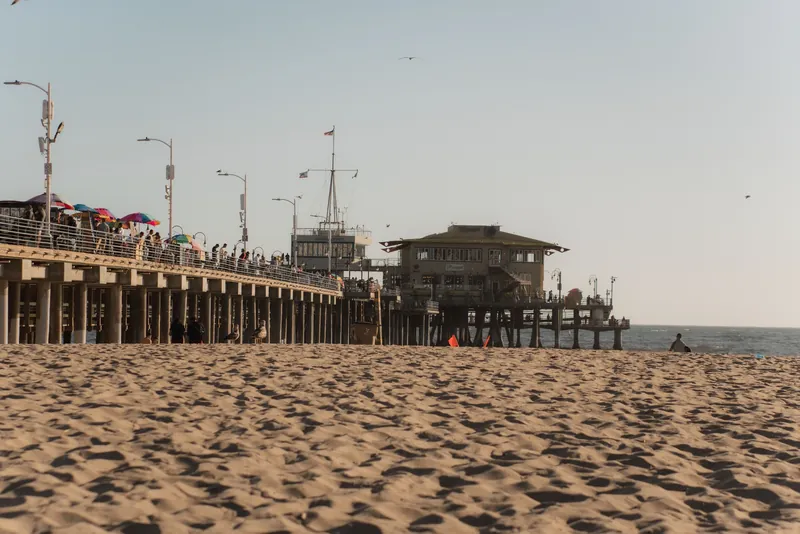 A scenic view of Santa Monica Pier with people enjoying the beach at sunset.