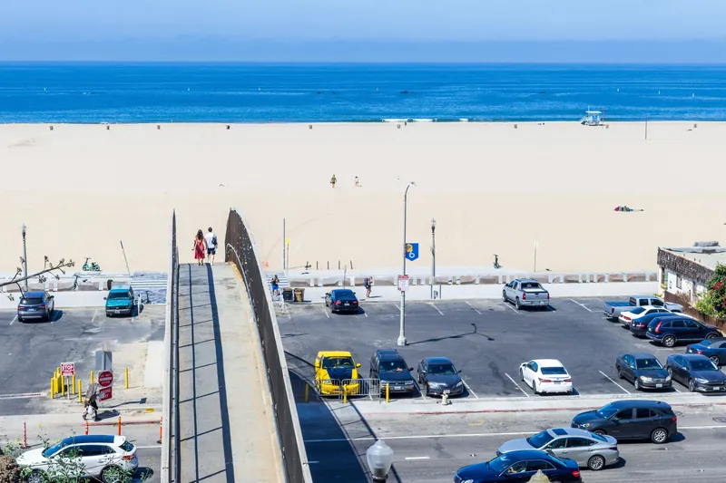 Aerial view of a coastal parking lot with footbridge leading to a serene beach.