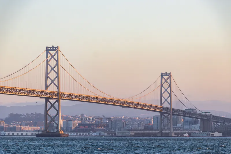 Majestic suspension bridge crossing rippling river against modern urban city on misty evening