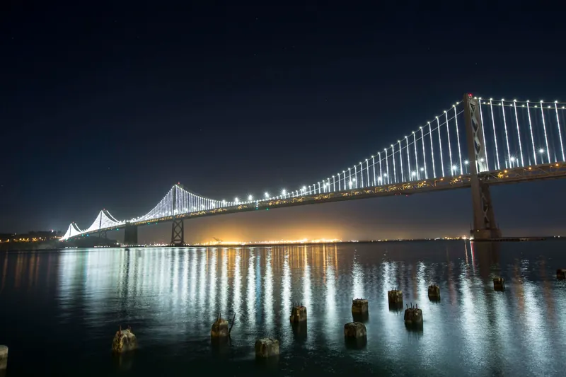 Stunning night view of the illuminated Bay Bridge reflecting in the calm waters.