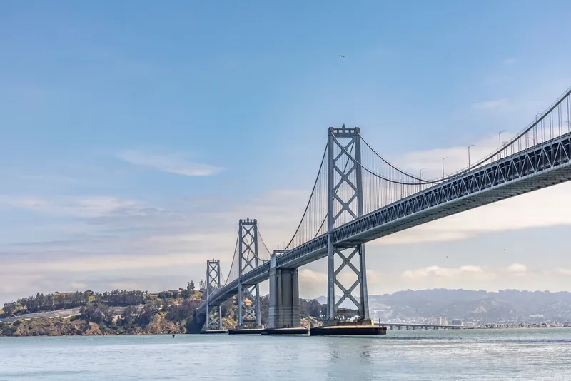 A stunning view of the San Francisco Bay Bridge extending over calm waters under a bright blue sky.